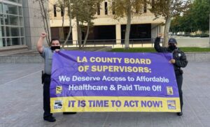 two people holding a banner addressing a call to action for the LA County Board